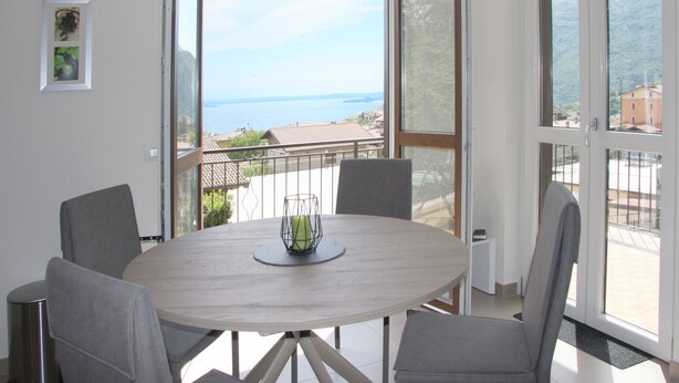 Una mesa redonda con cuatro sillas, un florero y vistas al mar a través de amplios ventanales.