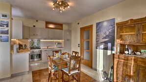 Una cocina moderna con armarios blancos, una mesa de comedor preparada para cuatro personas y un mueble de madera con botellas y copas.