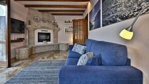 Un salón con sofá azul, chimenea, vigas de madera y un cuadro grande en la pared.