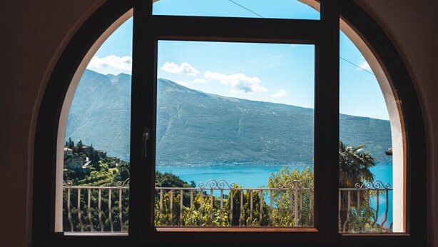 A view through a window with a balcony, overlooking a mountainous landscape and a body of water. - Armonia by Theater Home, with two parking spaces and beautiful lake view (Tignale)