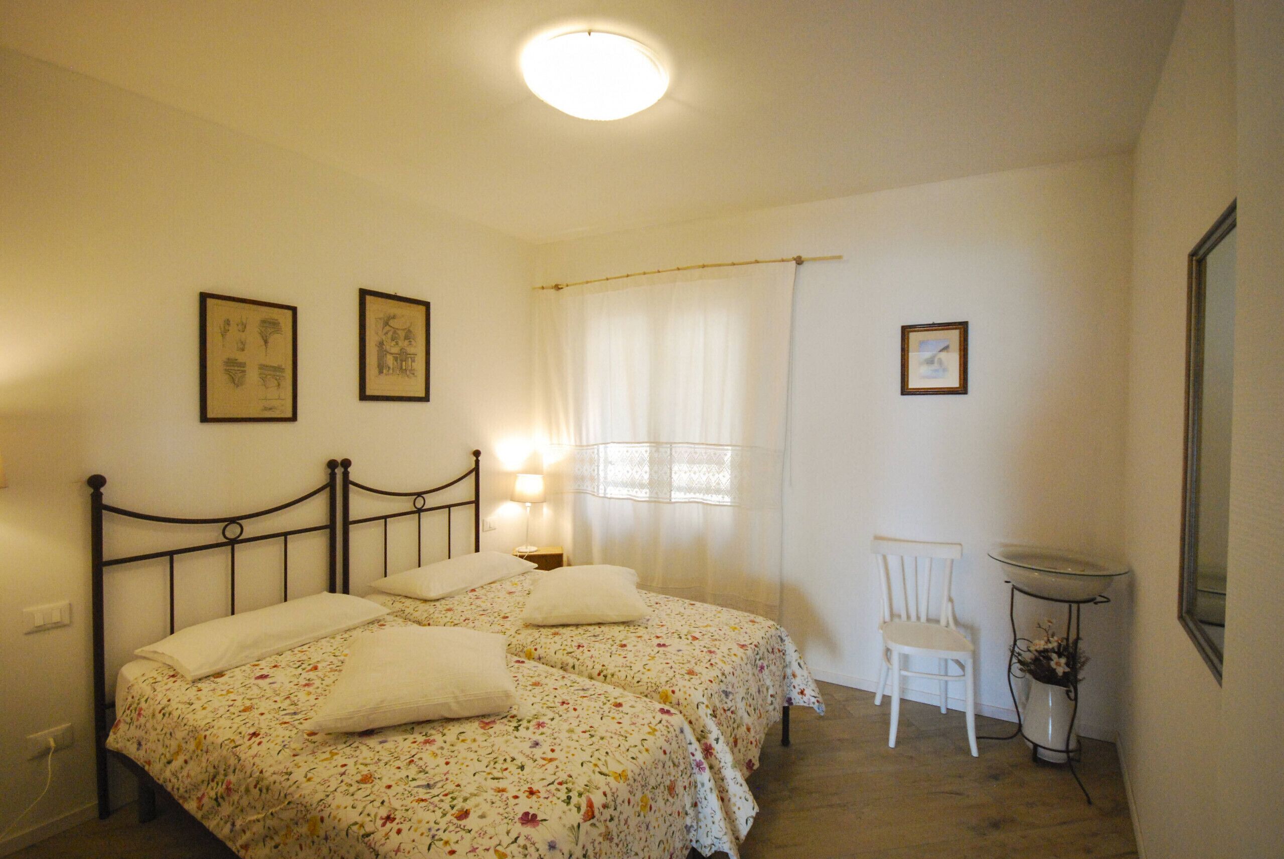 Ein Schlafzimmer mit zwei Betten, einem Sessel, einem Nachttisch und einem Fenster mit Vorhängen.