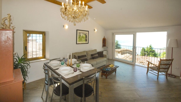 A spacious living area with a dining table set for four, a sofa, a chandelier, and a view of the outdoors. - Gina by Theater Home, in the historic centre with beautiful lake view (Tignale)