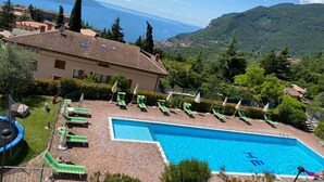 A hotel with a swimming pool, green lounge chairs, and a view of the sea and mountains. - Gina by Theater Home, in the historic centre with beautiful lake view (Tignale)