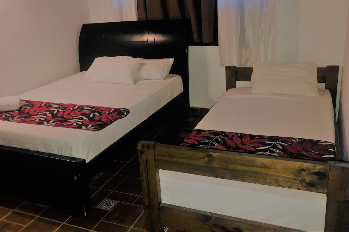 Duas camas de solteiro com cabeceiras pretas, roupa de cama branca e um cobertor com padrão floral na cama da esquerda.