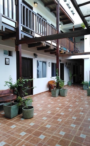 A covered courtyard with tiled flooring, potted plants, a wooden bench, and a balcony with railings. - Kayena Hostel (Santa Marta)