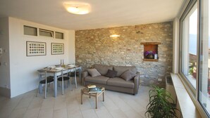 A living room with a stone wall, a sofa, a coffee table, and a dining area with chairs and a table. - Menèk by Theater Home, in the historic centre (Tignale)