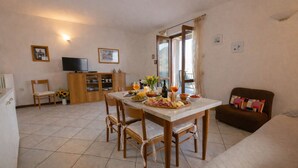 A living room with a dining table set for a meal, a television, and a sofa. - Michela 2 by Theater Home, with lake view (Tignale)