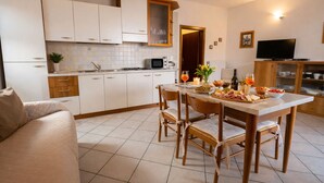 A compact kitchen with white cabinets, a dining table with chairs, a TV, and a cozy seating area. - Michela 2 by Theater Home, with lake view (Tignale)