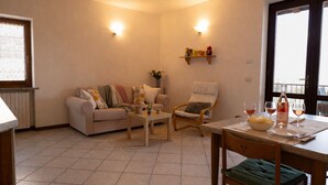 Un salon comprenant un canapé, un fauteuil, une table basse et une table à manger avec des verres à vin et une bouteille.