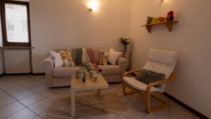 Un salon comprenant un canapé, une chaise en bois, une table basse, un radiateur, une fenêtre avec des stores et des lampes fixées au mur.
