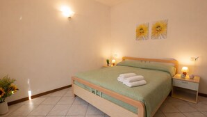 Une chambre à coucher comprenant un lit, deux lampes fixées au mur, une table de chevet, une plante en pot et deux œuvres d’art murales.