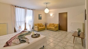 A bedroom with a bed, a sofa, a table with a vase, and a painting on the wall. - Michela 4  by Theater Home, with private garden and lake view (Tignale)