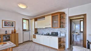 A compact kitchen with a central island, a dining area with a table and chairs, and a view into a bathroom. - Michela 4  by Theater Home, with private garden and lake view (Tignale)