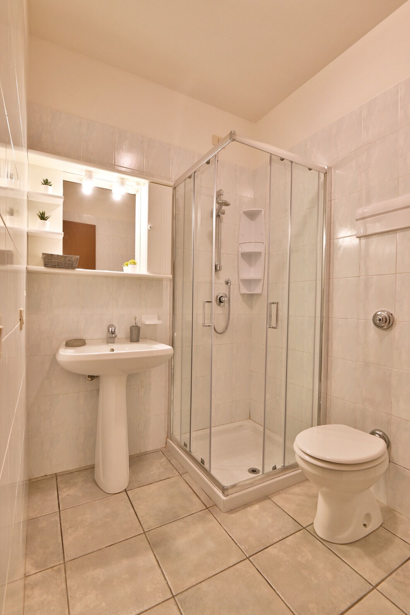 Une salle de bain avec une douche à parois de verre, un lavabo sur colonne et des toilettes.