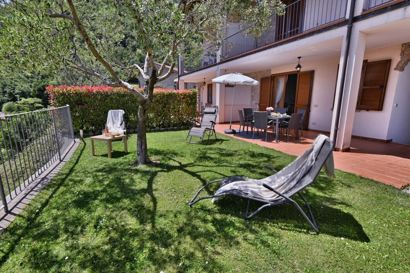 Ein gepflegter Garten mit Rasen, einem Baum und Gartenmöbeln, darunter ein Stuhl und ein Tisch.