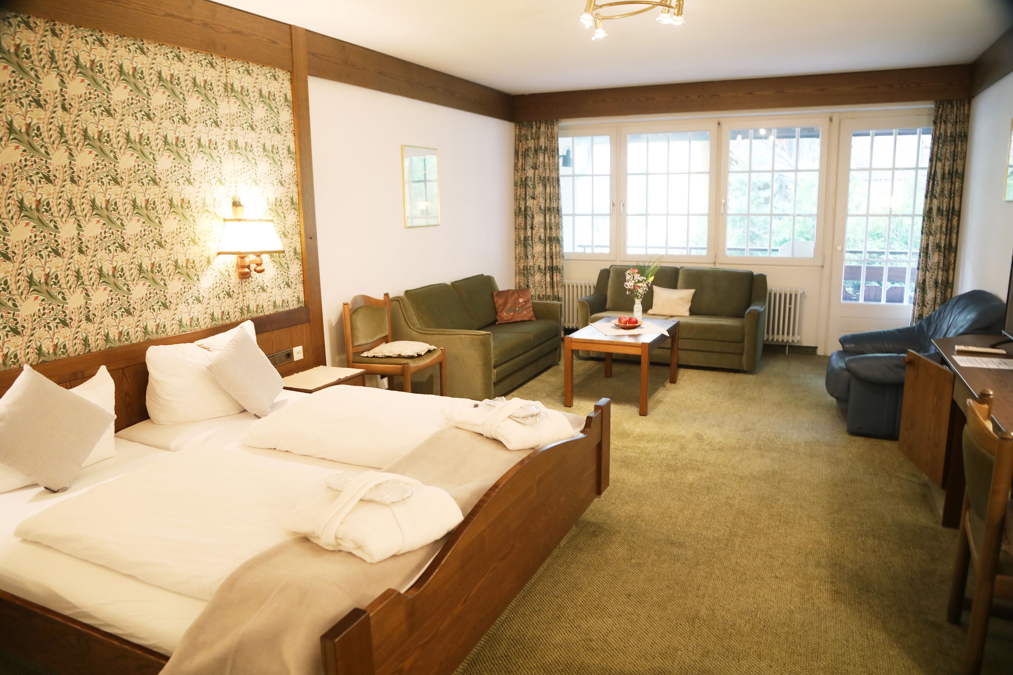 Ein Hotelzimmer mit einem großen Bett, zwei Sesseln, einem Sofa, einem kleinen Tisch und einem Fenster mit Vorhängen.