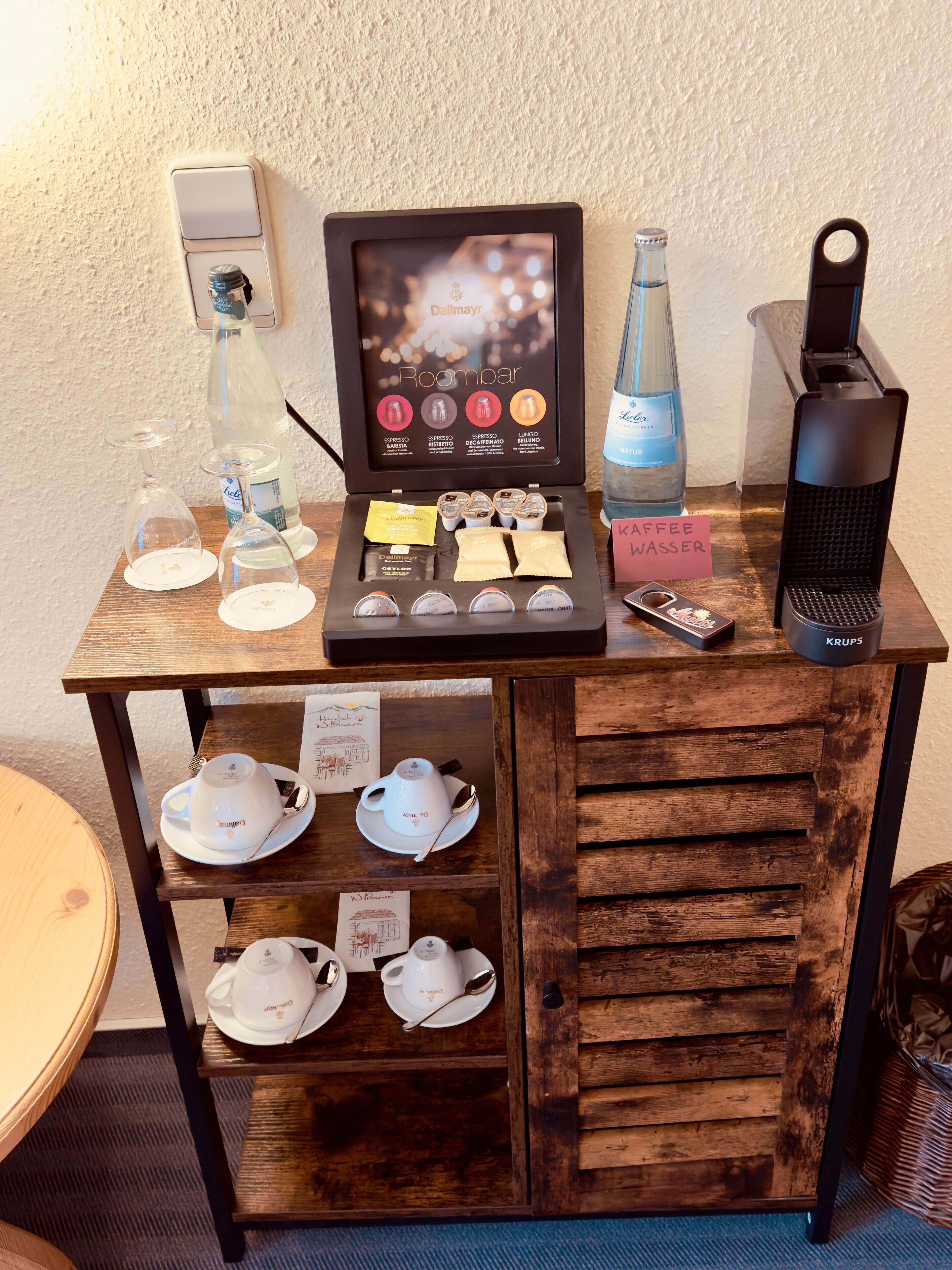 Una estación de café con una máquina de café, una variedad de cápsulas de café, un dispensador de agua y tazas de té.