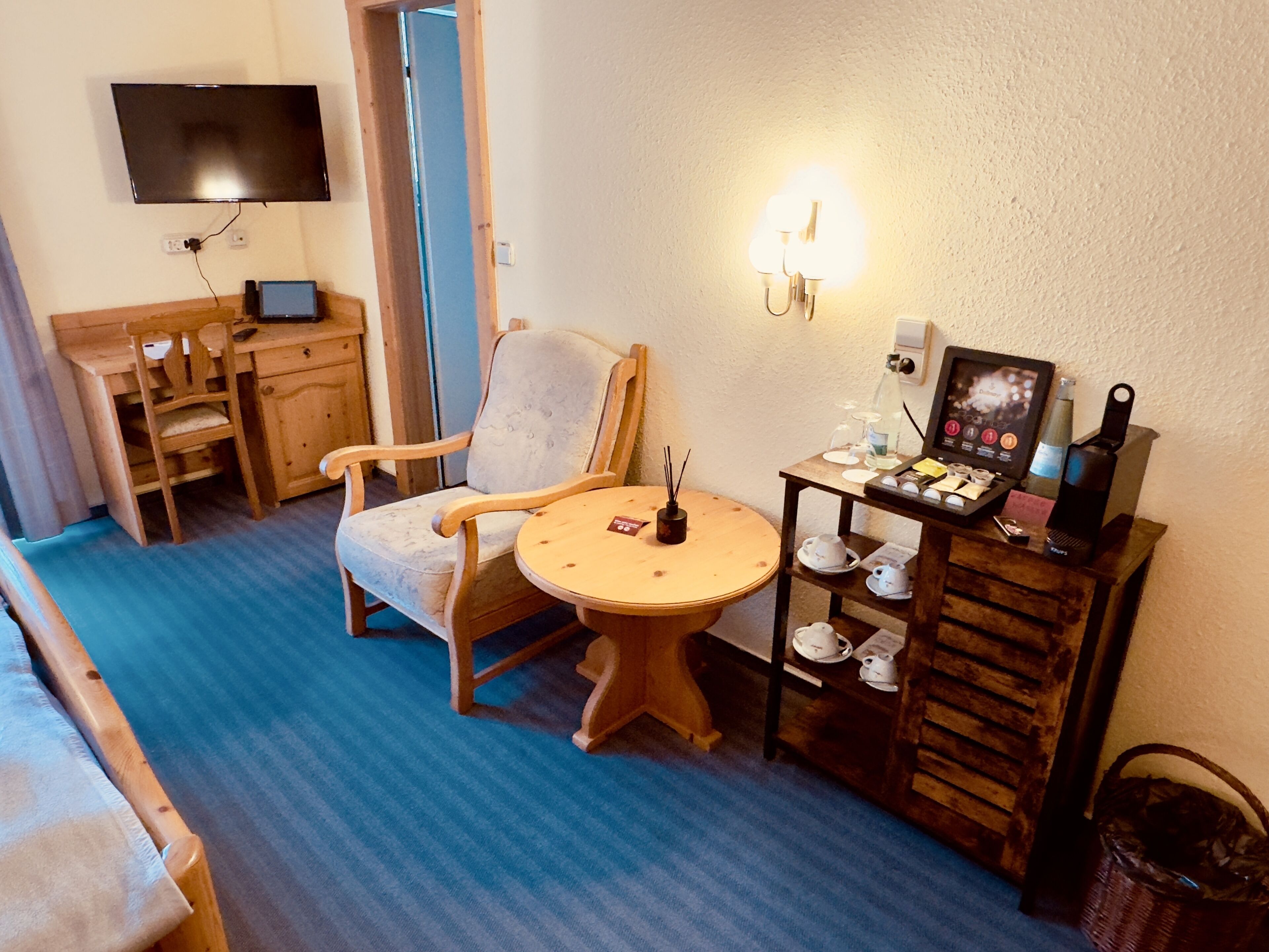 Ein gemütliches Zimmer mit einem Holzstuhl, einem kleinen runden Tisch, einem Fernseher und einer Wandleuchte.