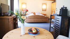 A hotel room with a wooden bed, a bedside table with a vase of flowers, a bowl of fruit, and a desk with a computer. - Adler Stube (Münstertal)