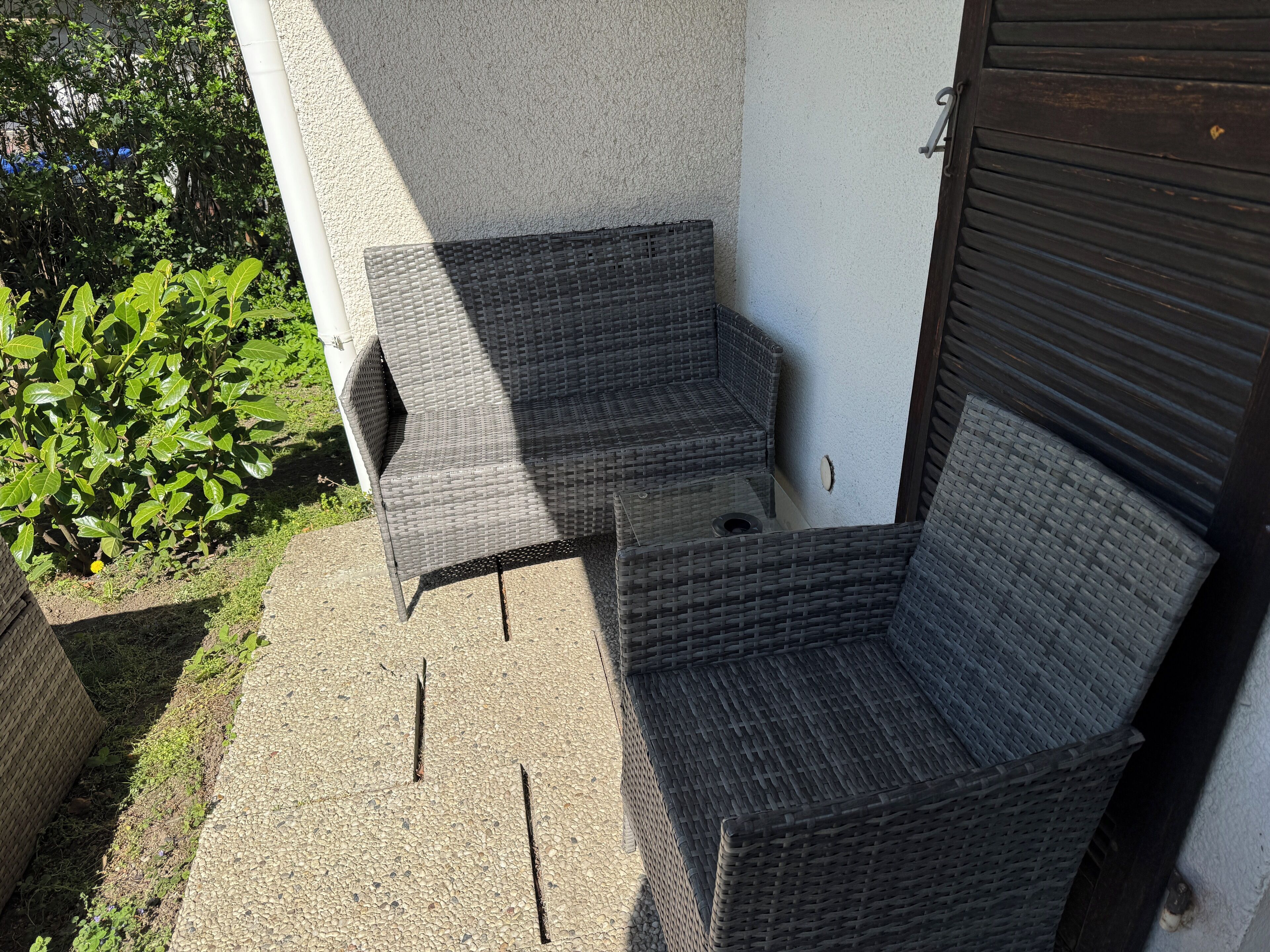 A corner seating area with two wicker chairs and a small table, adjacent to a building with a closed shutter.