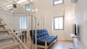 Et moderne interiør med trappe, blå sofa, TV på hylde og store vinduer.