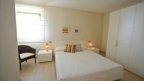 Une chambre à coucher avec un lit, deux tables de chevet avec des lampes, une chaise, une armoire et deux tableaux encadrés accrochés au mur.