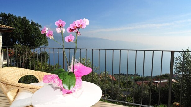Un balcon avec un fauteuil en osier, une table blanche et des orchidées roses.