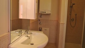 Une salle de bain équipée d’un lavabo, d’un miroir, d’un meuble de rangement, d’une douche et de toilettes.