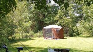 Piknik-alue, jossa on pöytä, penkkejä ja teltta, ja joka sijaitsee ruohikkoisella alueella puiden keskellä.