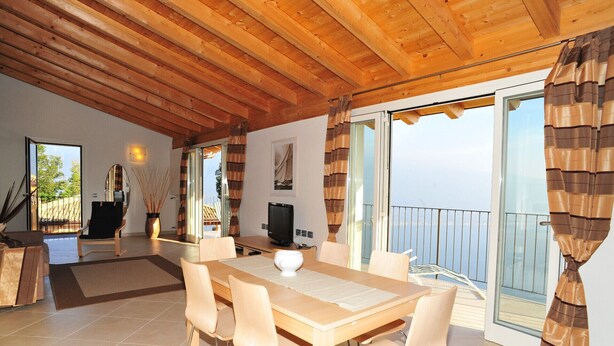 Un comedor amplio con una mesa y sillas de madera, un televisor y vistas al exterior a través de grandes puertas correderas de vidrio.