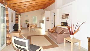 Un salón amplio con techo de madera, un sofá, un televisor y un comedor con mesa y sillas.