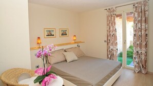 Un dormitorio con una cama, dos lámparas de pared, una silla de mimbre y una mesita con un florero.