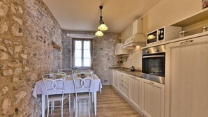 Une cuisine aux murs en pierre, une table à manger entourée de chaises blanches et un four moderne.