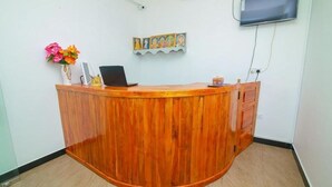 A reception desk with a laptop, a vase of flowers, and a wall-mounted TV. - Guest House Hotel Sun Blue (Alas Garden Trincomale Trincomale)