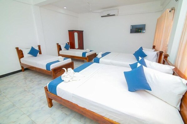 Four beds with white mattresses and blue bedding, a flat-screen TV, and a wooden wardrobe.