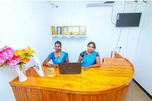 Welcome to our reception area, where friendly staff are available to assist with your stay. The area features a comfortable seating space, a reception desk with a laptop and telephone, and a decorative vase with fresh flowers.