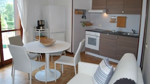 Een kleine keuken met een eethoek, een witte koelkast, een koffiezetapparaat en een spoelbak.