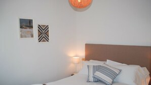 Een netjes opgemaakt bed met gestreepte kussens, een bruin hoofdbord en een witte deken. Er staat een wandlamp op het nachtkastje naast het bed.