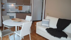 Een moderne keuken met witte kastjes, een fornuis en een eethoek met een witte tafel en stoelen.