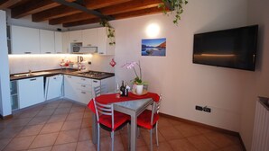 A compact kitchen with white cabinets, a tiled backsplash, a wooden ceiling, and a dining area with a red table and chairs. - Lince by Theater Home, with pool and lake view (Tignale)