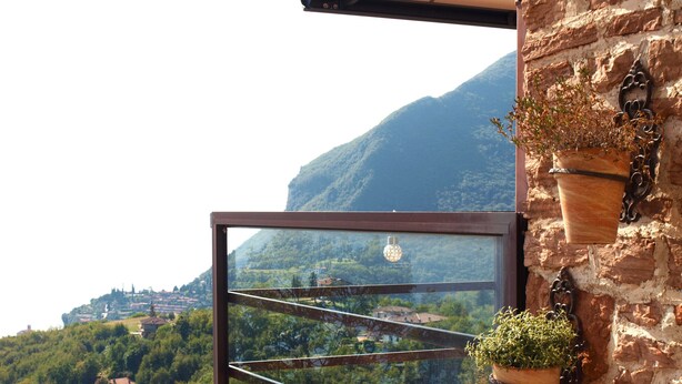 Een balkon met uitzicht op een bergachtig landschap, een hangende plant en een rustieke stenen muur.