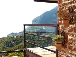 A balcony with a view of a mountainous landscape, a hanging plant, and a rustic stone wall. - Il Patio by Theater Home, with big terrace and marvellous lake view (Tignale)