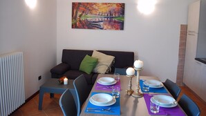 Un comedor con una mesa preparada para cuatro, un sofá con cojines, un cuadro en la pared y un radiador a la izquierda.
