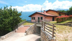 Una escalera de piedra conduce a una casa con techo rojo, rodeada de vegetación y con vistas a las montañas.
