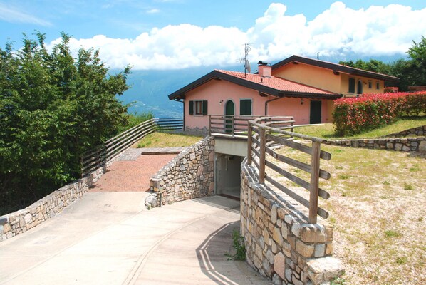 A stone staircase leading to a house with a red roof, surrounded by greenery and a view of the mountains.
