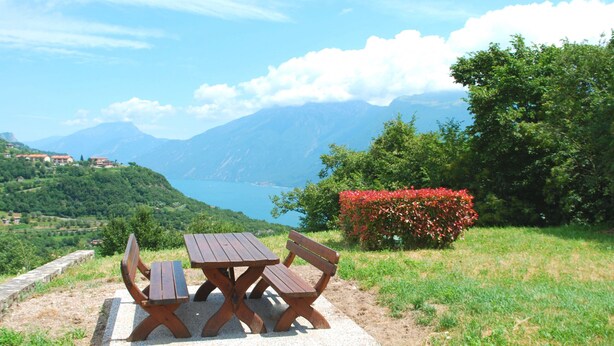 Mesa de picnic con bancos en un área verde con vistas a montañas y un lago.