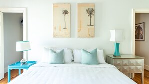 A bedroom with a bed, two nightstands, a lamp, and two wall art pieces. - Spacious Cottage w/ King Bed, Patio, Easy Parking by Lucky Savannah (Savannah)