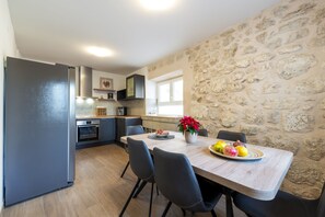 A modern kitchen with a stone wall, a dining table with chairs, and a refrigerator. - Villa Ane , infrared sauna, private pool, kids playground , Mediterranean garden (Mlini,Dubrovnik)
