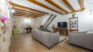 Un salón espacioso con pared de piedra, vigas de madera, una escalera, un televisor y dos sofás.