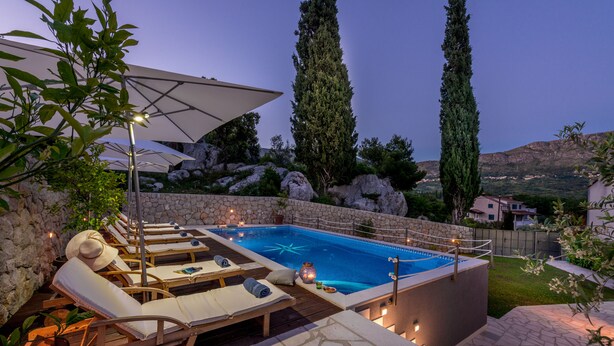 Un área de piscina privada con sillones de descanso, una sombrilla grande y un muro de piedra.
